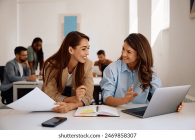 Happy businesswomen communicating while using laptop and working in creative office.  - Powered by Shutterstock