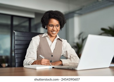 Happy busy young African American female manager wearing earbud having hybrid office business meeting by video conference call looking on laptop watching webinar or having online job interview. - Powered by Shutterstock