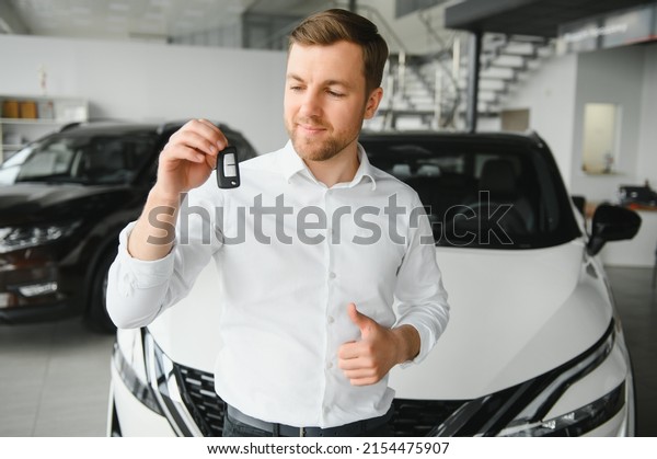 Happy buyer holding keys near the car in front\
of the modern avtosalon\
building.