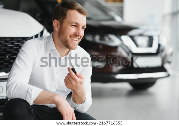 Happy buyer holding keys near the car in front
of the modern avtosalon
building.
