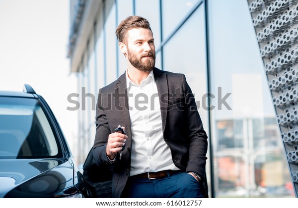 Happy buyer holding keys near the car in front\
of the modern avtosalon\
building