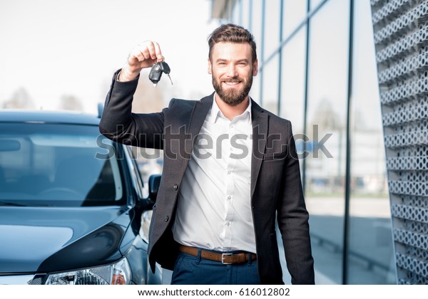 Happy buyer holding keys near the car in front
of the modern avtosalon
building