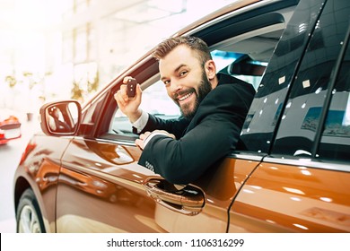 Happy buyer sitting in new car with keys in hand and looking on camera