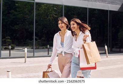 Happy buyers. Two female friends have a shopping day. Walking outdoors with bags.