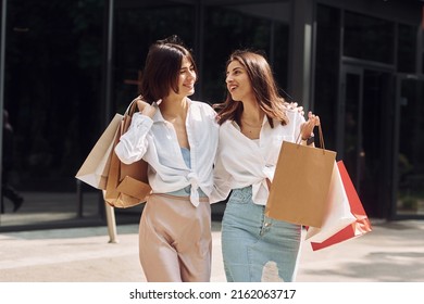 Happy buyers. Two female friends have a shopping day. Walking outdoors with bags.