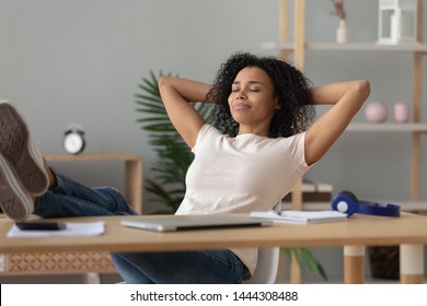 Happy calm african girl student relaxing holding hands behind finished study work breathing fresh air sit at home office desk feel stress relief stretching doing exercise dreaming enjoy peace of mind