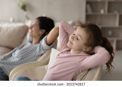 Happy calm little ethnic girl child and young Hispanic mother relax in armchair sleep or take nap on weekend. Relaxed small biracial daughter and Latino mom rest in chair daydream together at home.