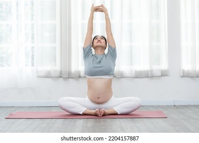 Happy Calm Pregnant Woman sit on yoga mat and stretching warm up for yoga practice,Pregnancy of young woman enjoy with yoga to breathing and meditation at home,Motherhood and Wellness Pregnant Concept - Powered by Shutterstock