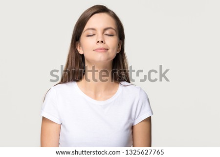 Happy calm teen girl enjoying good smell or pleasant fragrance, serene mindful young woman taking deep breath feel no stress free inhaling fresh air relaxing isolated on white grey studio background