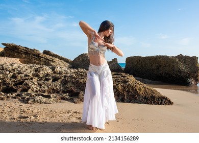 Happy and calm woman poses on the beach wearing the typical belly dance costume. Exotic beauty. Girl silhouette