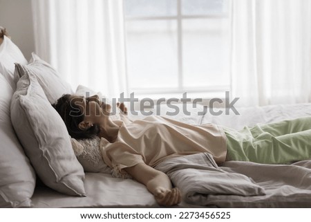Happy calm woman relaxing on soft amazing bed, lying on back with open arms on comfortable mattress, smiling with closed eyes, sleeping, awaking, enjoying recreation, good morning