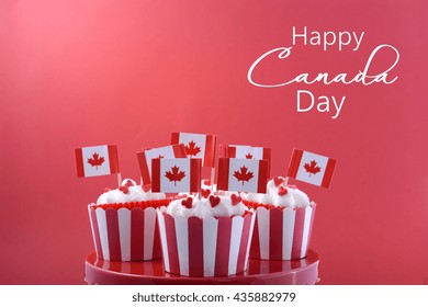 Happy Canada Day Party Cupcakes On A Red Cake Stand With Maple Leaf Flags On A White Wood Table And Red Background.