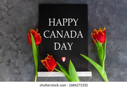 Happy Canada Day Text Written In A Chalkboard And Heart With Red And White Flag Colors On Grey Concrete Background With Fresh Tulips. Canadian Banner Concept. Blooming Flowers Flat Lay Greeting Card.