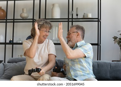 Happy Candid Older Senior Family Couple Giving High Five, Celebrating Winning Online Video Game. Emotional Laughing Middle Aged Man Woman Enjoying Leisure Activity, Pensioners And Modern Technology.