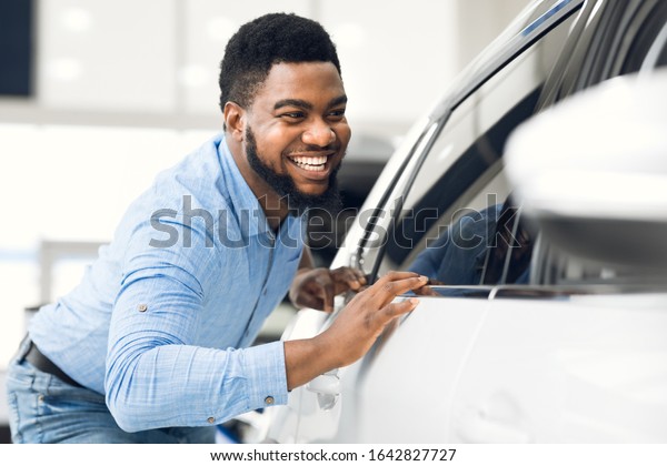 Happy Car Buyer. African\
American Guy Touching His New Auto In Dealership Showroom.\
Selective Focus