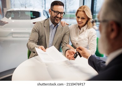 Happy car buyer with his beautiful wife taking car keys while sitting in car salon. - Shutterstock ID 2110476917