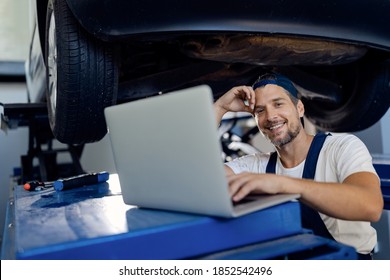 Happy car mechanic using laptop while working at auto repair shop and looking at camera. - Powered by Shutterstock