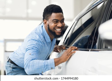 Happy Car Owner. African Guy Touching His New Vehicle Excited About Buying Automobile In Dealership Showroom. Selective Focus
