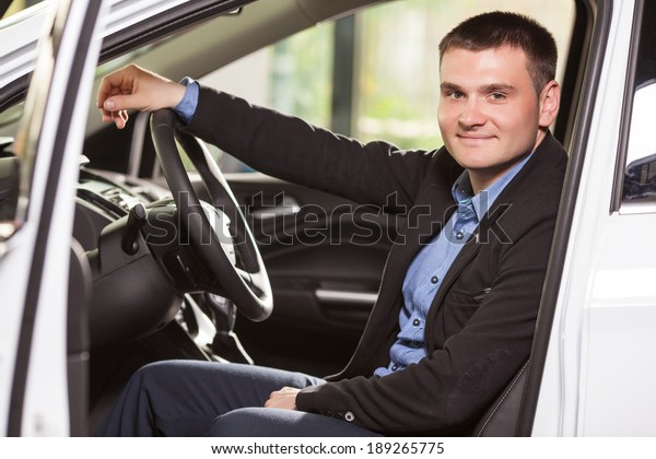 Happy car owner at the\
dealership. Handsome young men sitting at front seat of the car\
looking at camera