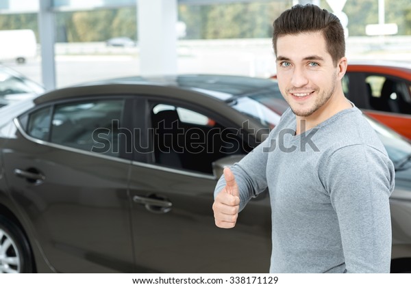 Happy car owner.
Half length portrait of a handsome man smiling happily and showing
thumbs up in a car salon