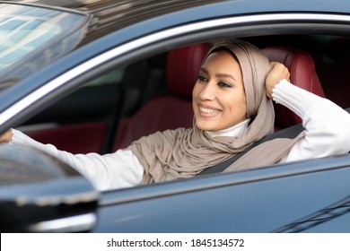 Happy Car Owner. Portrait of carefree smiling arabic lady in headscarf driving new luxury car. Cheerful muslim woman wearing hijab sitting in salon on driver' seat, holding steering wheel