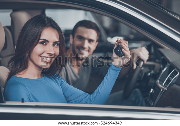 Happy\
car owners. Beautiful young couple sitting at the front seats of\
their new car while woman showing keys and\
smiling