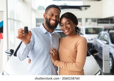 Happy Car Owners. Portrait Of Young Black Couple With Automobile Keys In Hands Posing In Modern Dealership Center After Purchasing Their Own Vehicle, African American Family Smiling At Camera