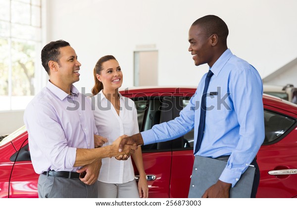 happy car\
salesman handshaking with middle aged\
buyer