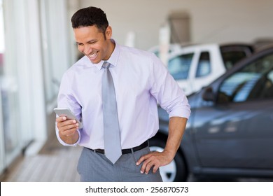 Happy Car Salesman Using Smart Phone In Showroom