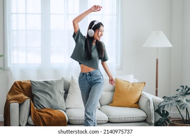 Happy carefree asian woman wearing headphones have fun moving listening to music relax in living room, She dance enjoy leisure weekend at home. - Shutterstock ID 2140975737