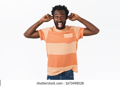 Happy, carefree bearded african-american guy having fun, not scared being funny and cute, showing hilarious faces, grimacing playfully, pulling ears and stick tongue as smiling, white background