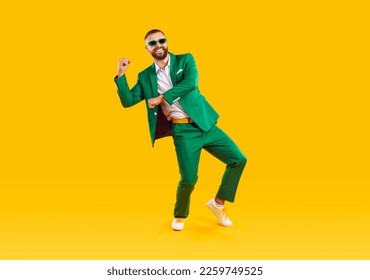 Happy carefree handsome young man in trendy green suit and sunglasses celebrating St Patrick's Day, having fun and dancing on yellow colour studio background. St Patrick's Day and fashion concept - Powered by Shutterstock