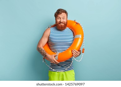 Happy Carefree Male With Life Preserver, Has Glad Reaction, Grins At Camera, Stands In Casual Clothes, Isolated Over Blue Backgound. Cheerful Foxy Sailor With Swimming Equipment. Safety Concept