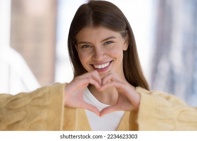 Happy carefree pretty girl in casual showing finger heart shape, symbol of love, romance, happiness. Blogger, influencer woman girl sharing emotions, making hand like gesture, smiling at camera - Powered by Shutterstock