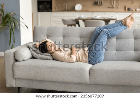 Happy carefree relaxed Indian woman resting on cozy sofa with legs on soft back, smiling with closed eyes, laughing, enjoying relaxation, leisure comfort in home interior