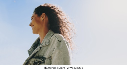 Happy, carefree woman smiling while enjoying a joyful day outdoors with the blue sky in the background. Side profile of a happy woman smiling on a sunny day. - Powered by Shutterstock