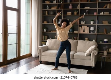Happy carefree young African American woman dancing on floor carpet, listening energetic disco in living room, laughing enjoying hobby leisure time, celebrating freedom or moving into own home.