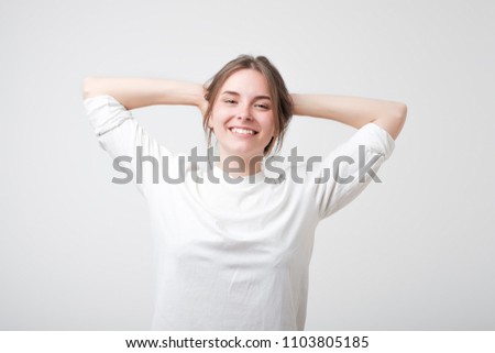 Happy carefree young caucasian woman in white t-shirt with a cute grin posing with her hands over her head. Concept of success and carefree emotion.