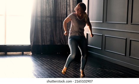 Happy Carefree Young Woman Dancing Alone In A Dark Room With A Large Window, Enjoying A New Hit Song, Having Fun At Home