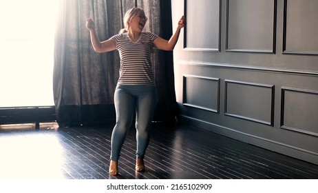 Happy Carefree Young Woman Dancing Alone In A Dark Room With A Large Window, Enjoying A New Hit Song, Having Fun At Home