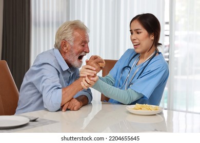 Happy Caregiver Try Stopping Senior Caucasian Man Eating Hamburger Or Junk Food And Taking Medicine After Breakfast In Living Room At Retirement House. Unhealthy And Junk Food Lifestyle Concept
