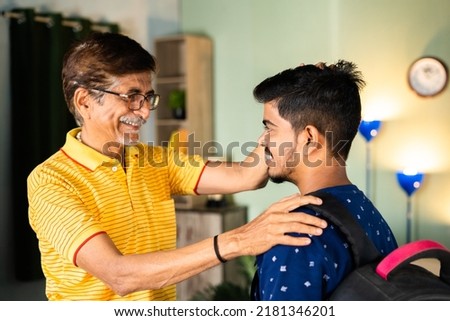 Happy caring grandfather blessing school going grandson with backback at home - concept of parental appreciation, achievement and elderly encouragement