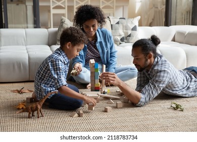 Happy caring loving young African American couple parents playing wooden toys with small cute multiethnic child son, enjoying creative playtime activity together in modern living room, childcare