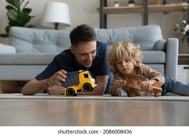 Happy Caring Millennial Dad And Sweet Preschool Son Kid Lying On Heating Floor, Playing Transport, Toy Truck, Wooden Airplane, Having Fun Together. Father And Son Enjoying Leisure Time Together