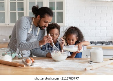 Happy caring young African American father teaching small adorable kids son daughter mixing flour with milk, enjoying preparing dough for homemade pastry, cooking together in modern kitchen. - Powered by Shutterstock