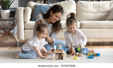 Happy caring young Caucasian mother have fun play with small daughter at home in living room. Smiling loving mom feel playful engaged in game activity with blocks bricks with little girls children.