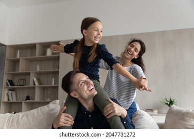 Happy caring young hispanic latino family couple having fun with joyful adorable small adopted preteen kid girl, enjoying entertaining domestic activity game, weekend playful pastime at home.