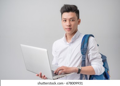 Happy Casual Asian Male Student Using Laptop Isolated On A Gray Background