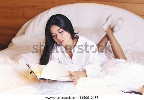 Happy casual\
beautiful woman lying relax on the bed in the bedroom at\
house.attractive woman read book on\
bed.