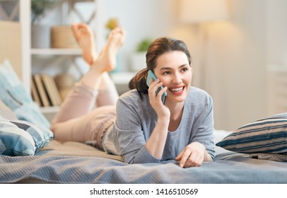 Happy casual beautiful woman is talking on a phone sitting on the bed in the house. - Powered by Shutterstock